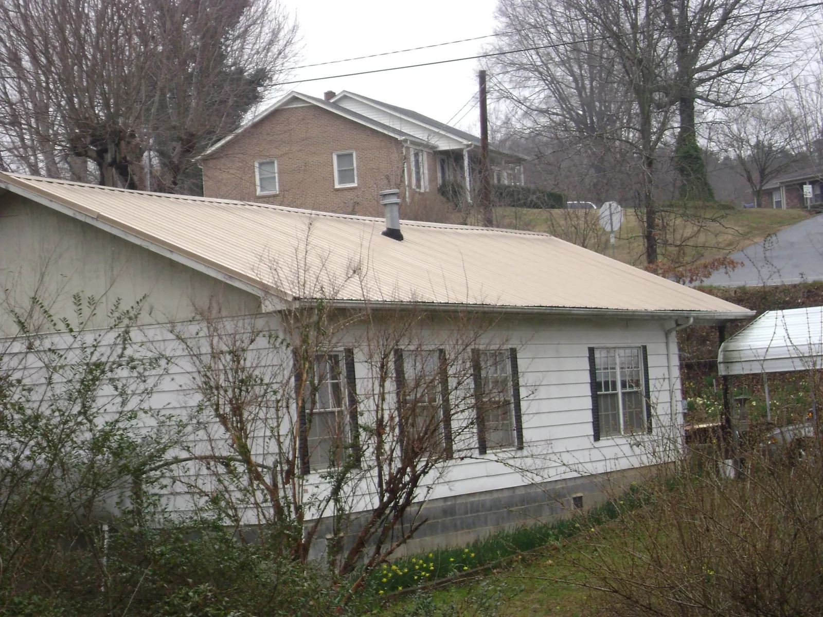 Tan metal roof on a white sided house set into a hillside — Commercial Roofing by Roofing Brothers in Sandwich